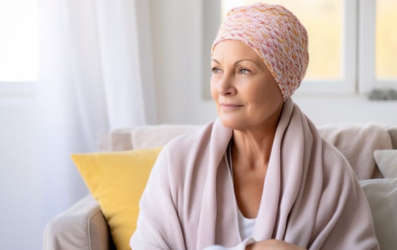 Woman with a head wrap sitting in her lounge, looking out of the window with a knowing smile