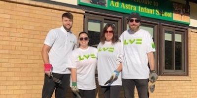 Four happy volunteers in LV branded T shirts, standing outside an infant school holding trowels