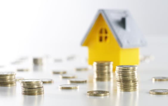 yellow model house with a grey roof with coins piled up next to it