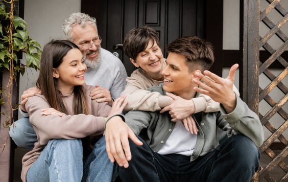 Smiling young man talking to family and sister while sitting on porch of house