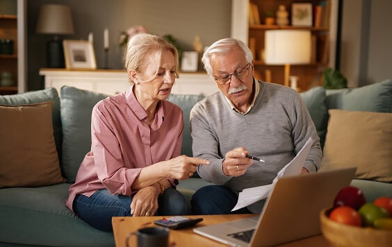A Caucasian elderly couple sit on a blue sofa in their living room.
