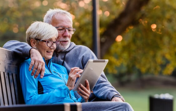 Older couple on a tablet outside on a bench