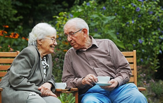 Older couple drinking tea outside on a bench