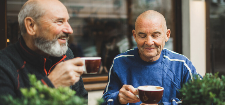 Two older men drinking coffee outside a cafe