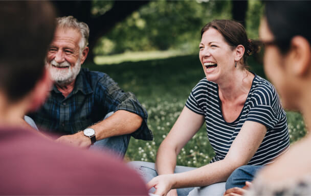 Happy senior woman and man sat in a park laughing with a group of friends