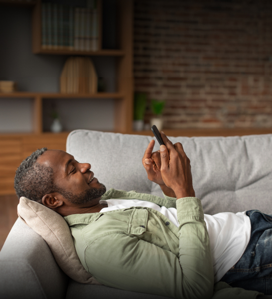 Happy man laying back on the sofa, using his phone