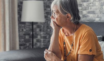 Older woman looking mournfully out of a window. 