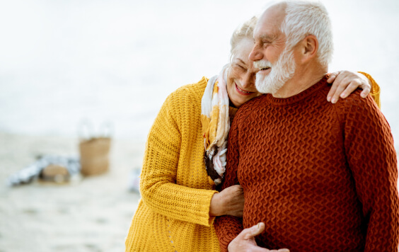 Portrait of a happy senior couple dressed in colourful sweaters hugging on the sandy beach