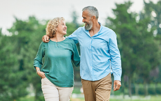 Older couple walking outside with trees in the background
