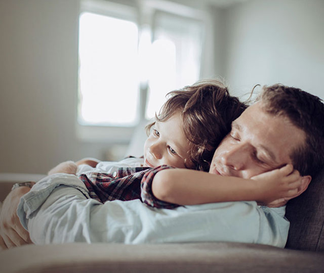 Sleepy father holding child, resting on the sofa