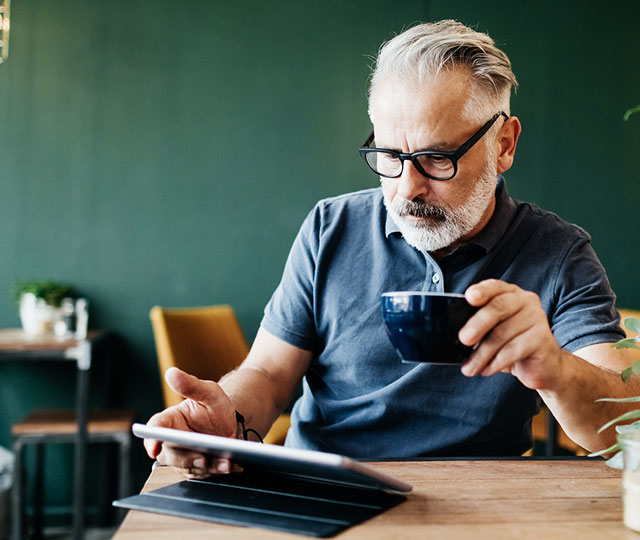 Man drinking a coffee and reading on a tablet
