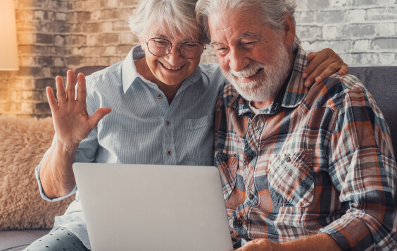 Cute couple of old people sitting on the sofa using laptop together shopping and surfing the net