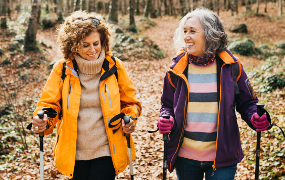 Two senior female friends hiking together through the forest in autumn