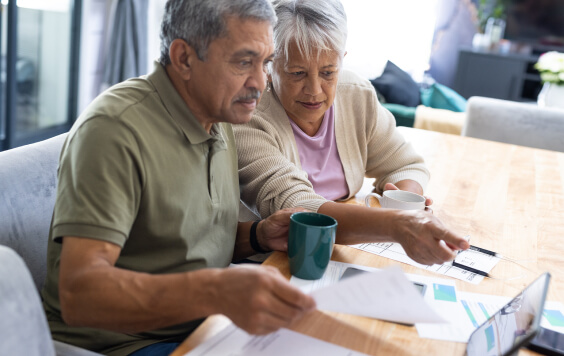 Biracial senior couple with coffee cups discussing bills and expenses on table at home 