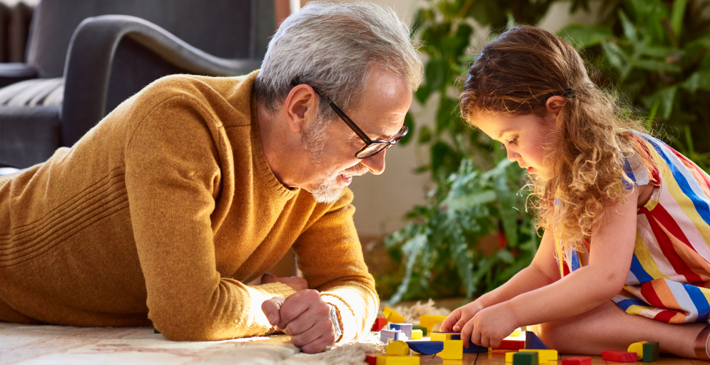 Granddaughter playing with wooden block and granddad watching