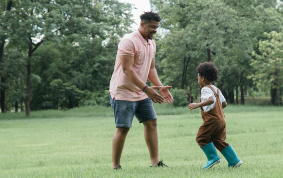 Happy father in shorts and a t shirt reaching down to lift a playful child