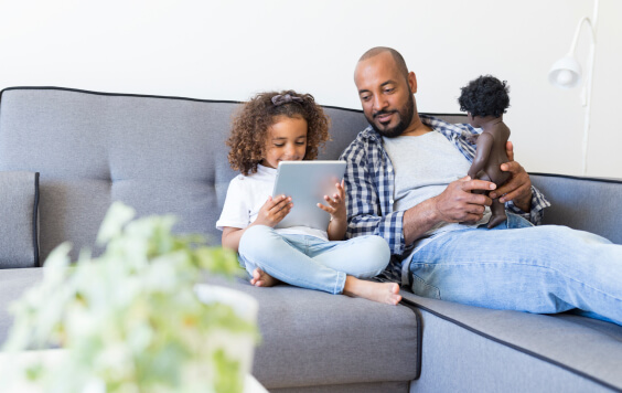 Father and daughter on sofa holding a doll and a tablet