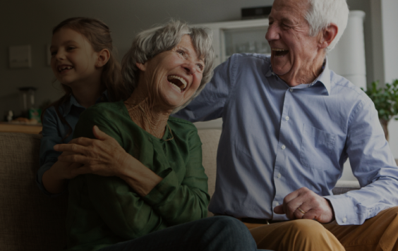 elderly couple laughing with child on a sofa