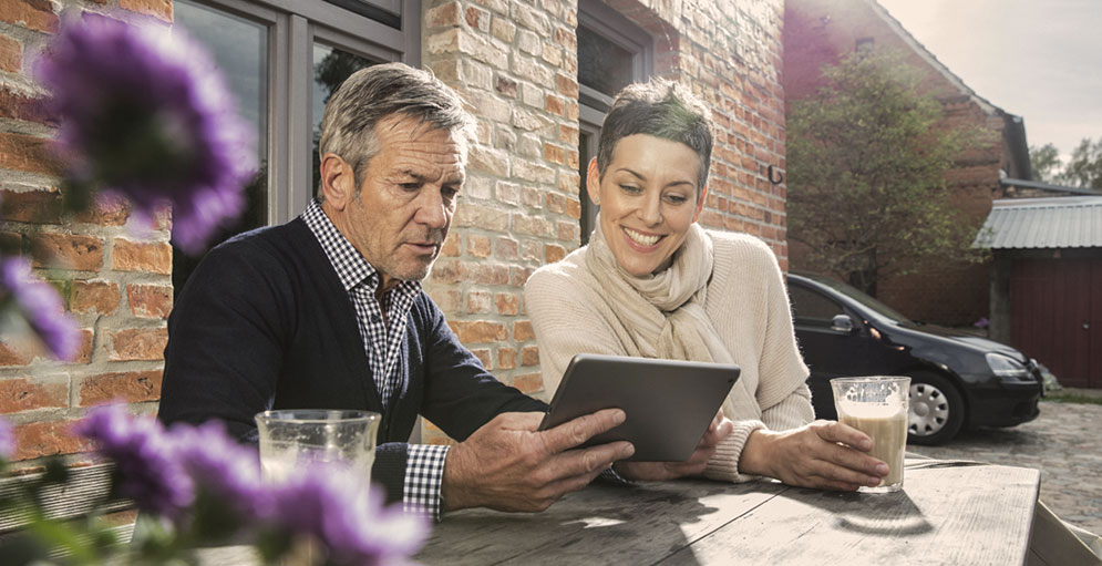 Two people look at a tablet in a sunny beer garden