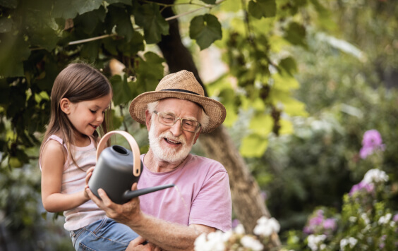 Little girl helping her grandpa watering plants