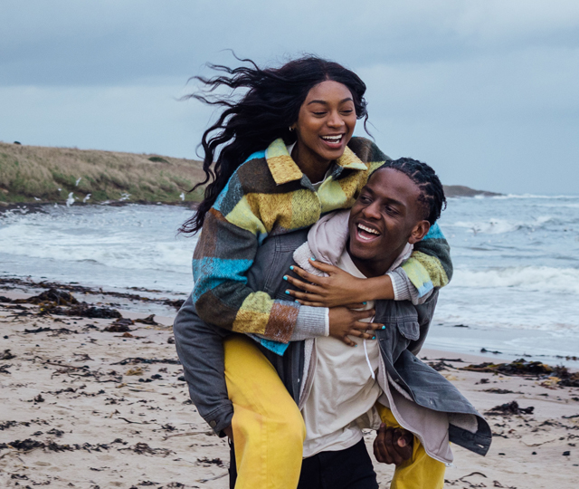 Happy man in his thirties giving his partner a piggy back on a windy beach