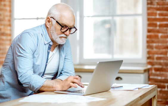 Handsome senior man dressed in blue shirt working with laptop at home
