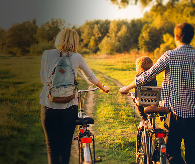 Man and woman pushing bikes with child in green field