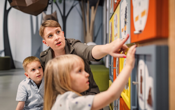 Mother playing discovery games with two little children in an interactive natural history museum exhibition