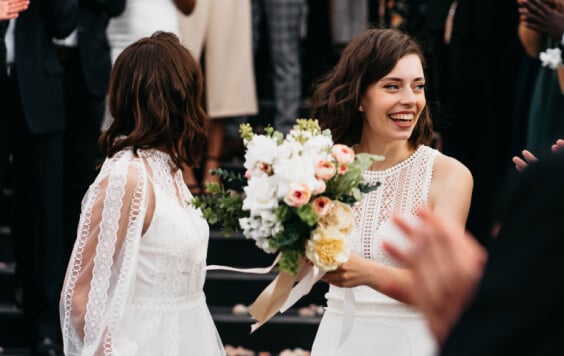 Candid shot of two female lesbian LGBT brides walking down the stairs during their wedding ceremony as guests throwing rose petal
