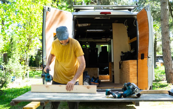 Carpenter working on wood plank, building camper van in nature