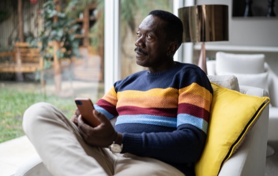 Man sitting in an armchair contemplating and using smartphone