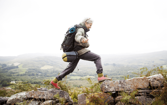 Older adult woman stepping over a gap in a stone wall in the countryside