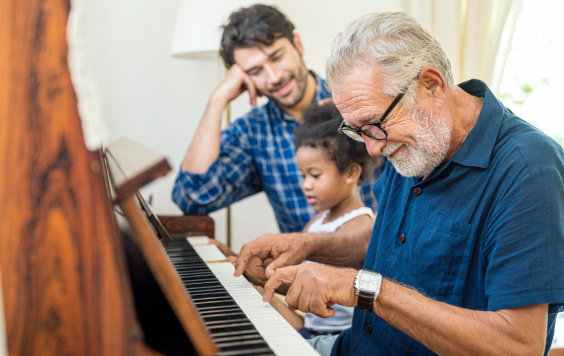 Grandad with adult son and granddaughter sitting at a piano