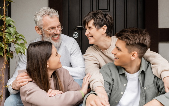 positive middle aged parents talking while hugging children and sitting on porch of house