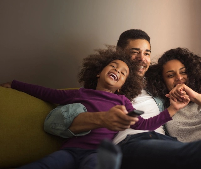 Family laughing on sofa watching TV