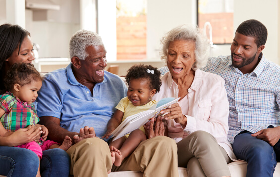 Multigenerational family sat on a sofa ready books to two toddlers