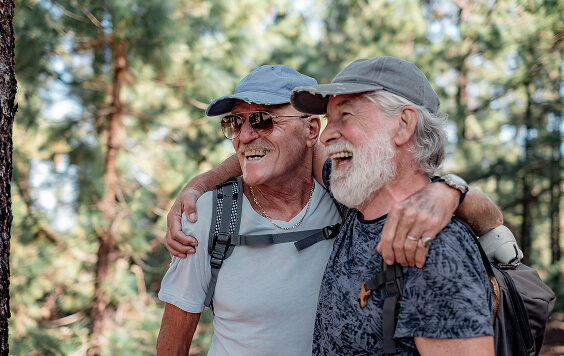 Two older males hugging outside in a forest area