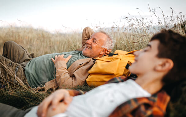 Grandfather and Grandson laying in a field after hiking to hilltop