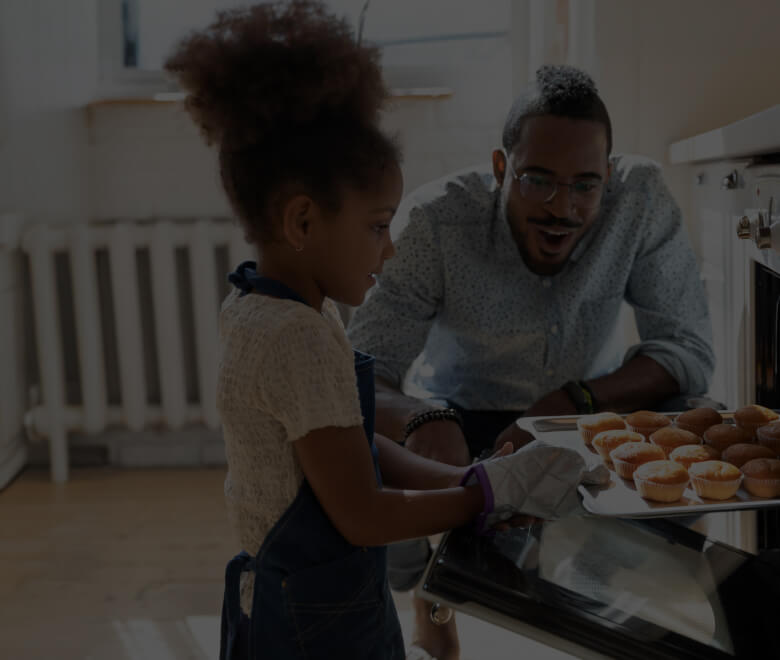 Excited dad watching daughter take self baked cakes out of the oven