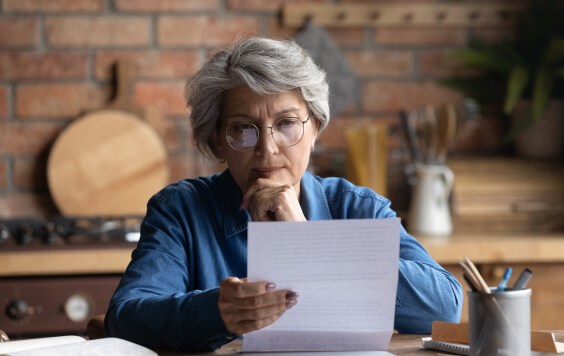 Thoughtful middle aged 60s woman in eyeglasses reading paper letter carefully