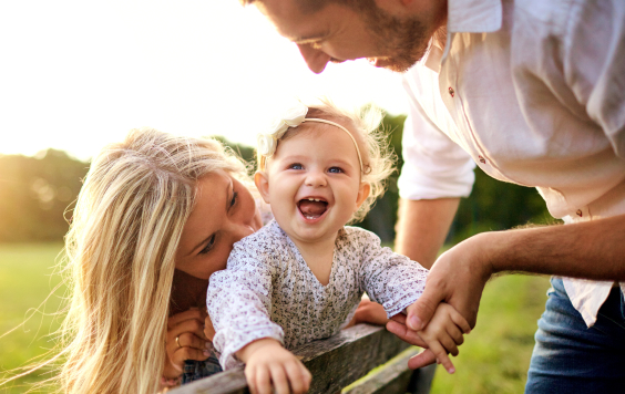 Happy family in a park in summer autumn. Mother, father and baby play in nature in the rays of sunset.