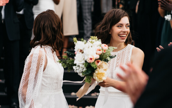 Candid shot of two female lesbian LGBT brides walking down the stairs during their wedding ceremony as guests throwing rose petal