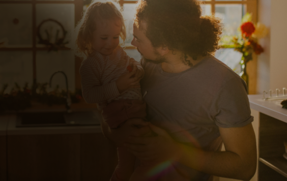father holding daughter in sun lit kitchen