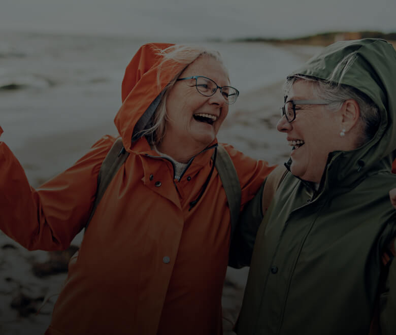 Two happy older women walking on a beach in their rain coats on a stormy day
